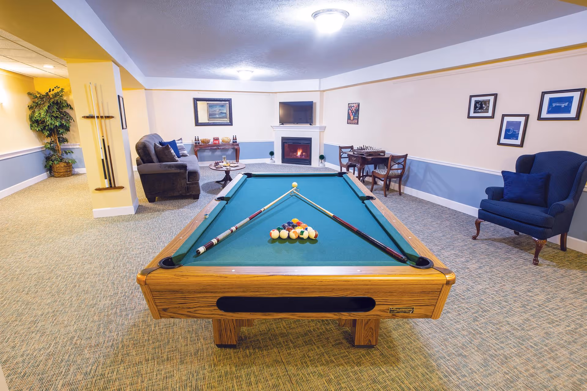 A spacious recreation room with a pool table centered, seating areas, a fireplace and framed artwork on the walls.