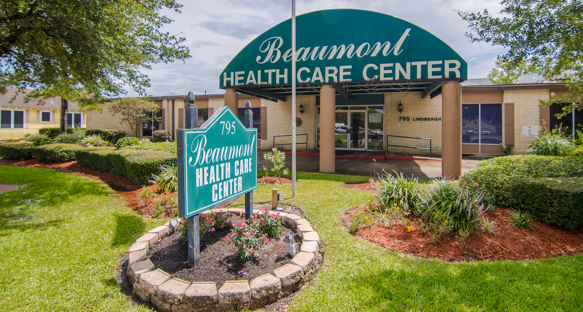 Front entrance of Beaumont Health Care Center with a green awning and a landscaped sign in front.