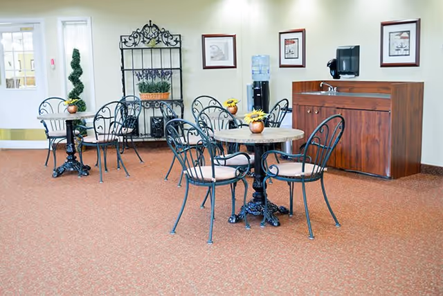 Small communal dining area with round tables and wrought-iron chairs, a water cooler and sink cabinet against the wall.