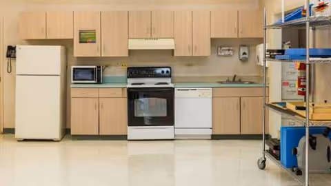 A compact kitchen in a senior living facility with fridge, stove, and cabinets.