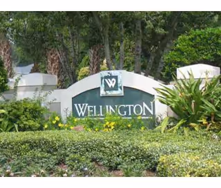Entrance stone sign reading 'Wellington' set among landscaped shrubs and trees.