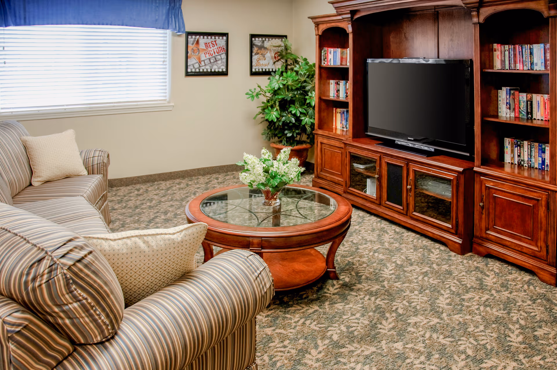 Comfortable living room with striped sofas, a round glass-top coffee table, and a large wooden entertainment center with TV and bookshelves.