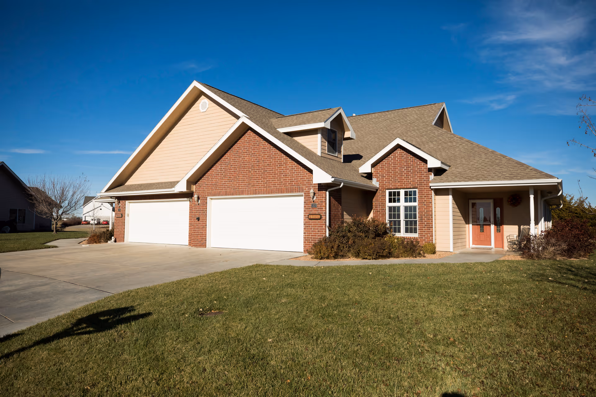 Single-story brick-and-siding suburban house with a three-car garage, driveway, and front lawn under a blue sky.