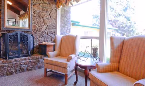 Cozy seating area with beige armchairs, a small table, and a stone fireplace by a window.