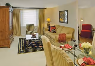Well-lit living room with a sofa, armchairs, glass-top dining table set, TV armoire, and decorative accents.