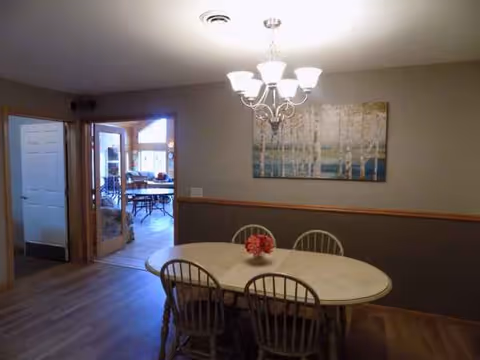 Interior dining room with a round table, four chairs, chandelier, and wall art.