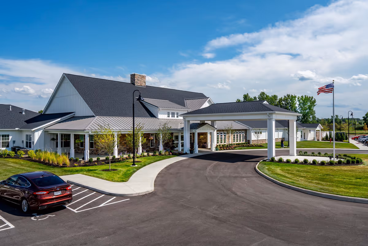Front exterior of Walnut Crossing with a covered porte-cochere, circular driveway, landscaped grounds, and an American flag.