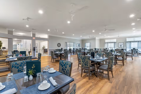 Bright, spacious dining room with multiple set tables, patterned upholstered chairs, and wood floors.