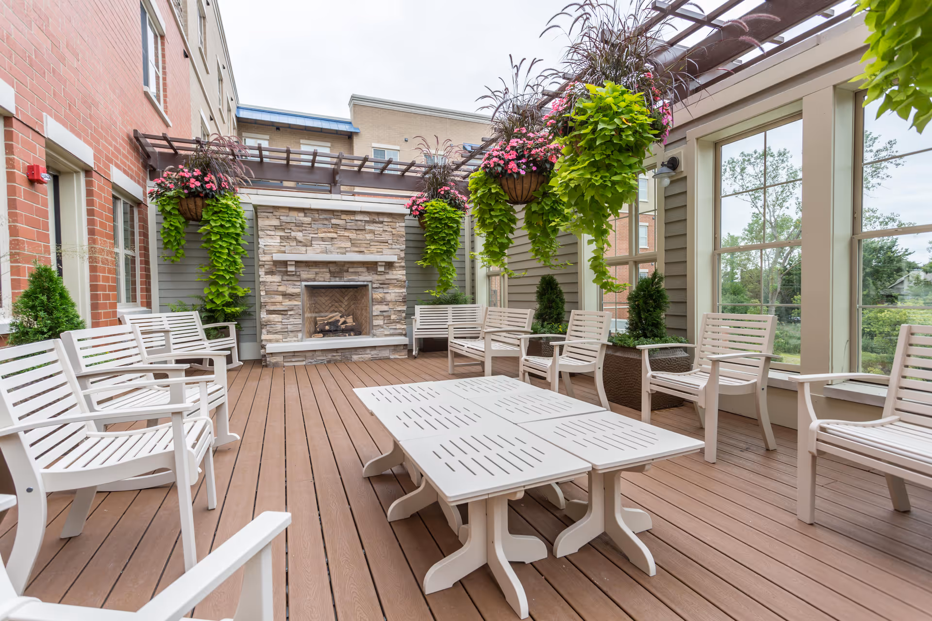 Outdoor covered patio with white chairs and tables, a stone fireplace, and hanging flower baskets.