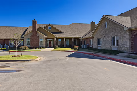 Front view of a senior living facility with stone exterior and circular driveway.