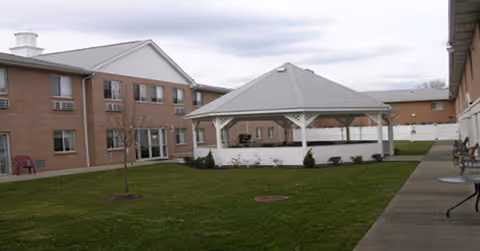 Courtyard of a brick senior living facility with a white gazebo and lawn between two building wings.