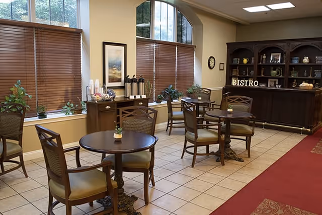Small bistro-style dining area with round tables and chairs, a service counter labeled "BISTRO", and large windows with wooden blinds.