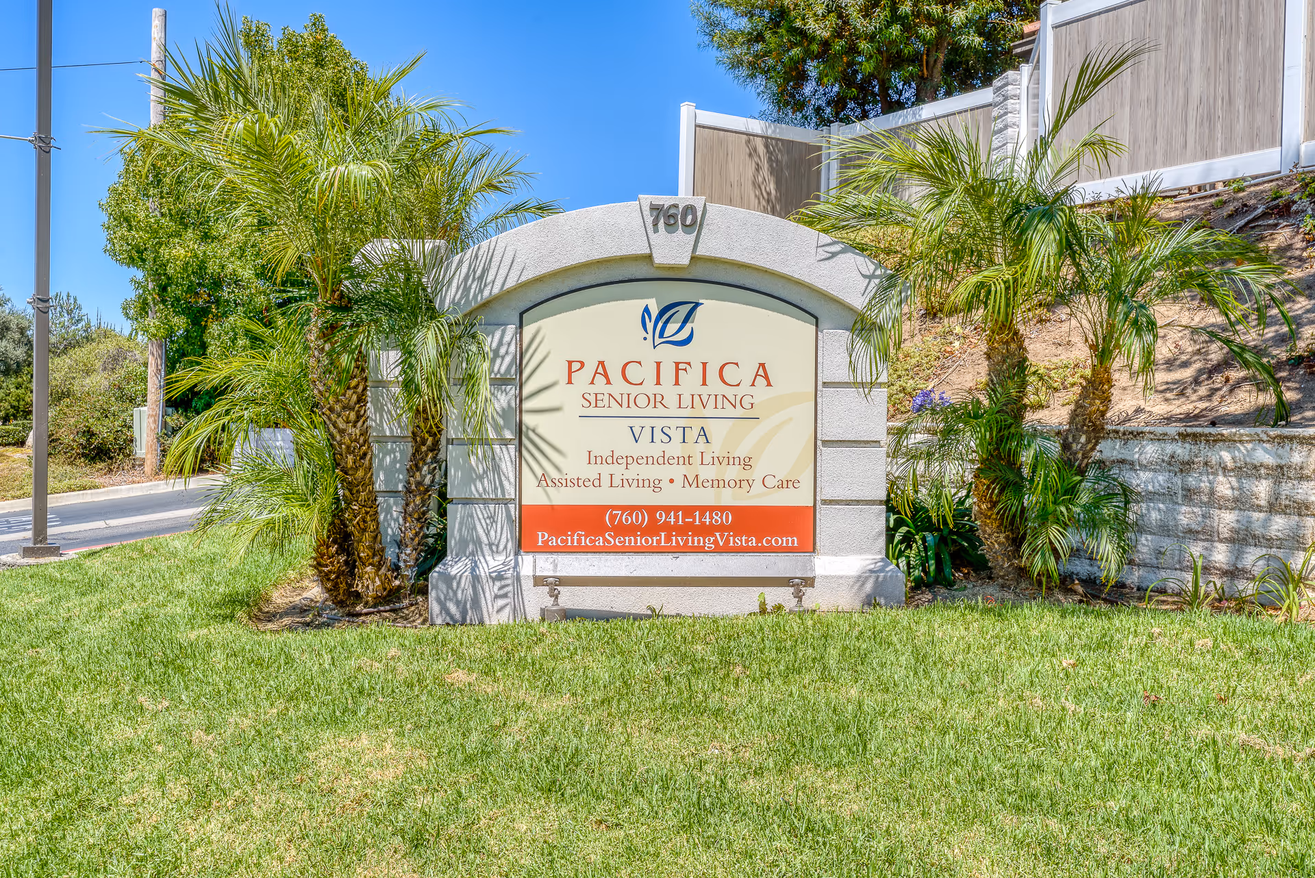 Entrance sign for Pacifica Senior Living Vista on a grassy lawn flanked by palm trees.