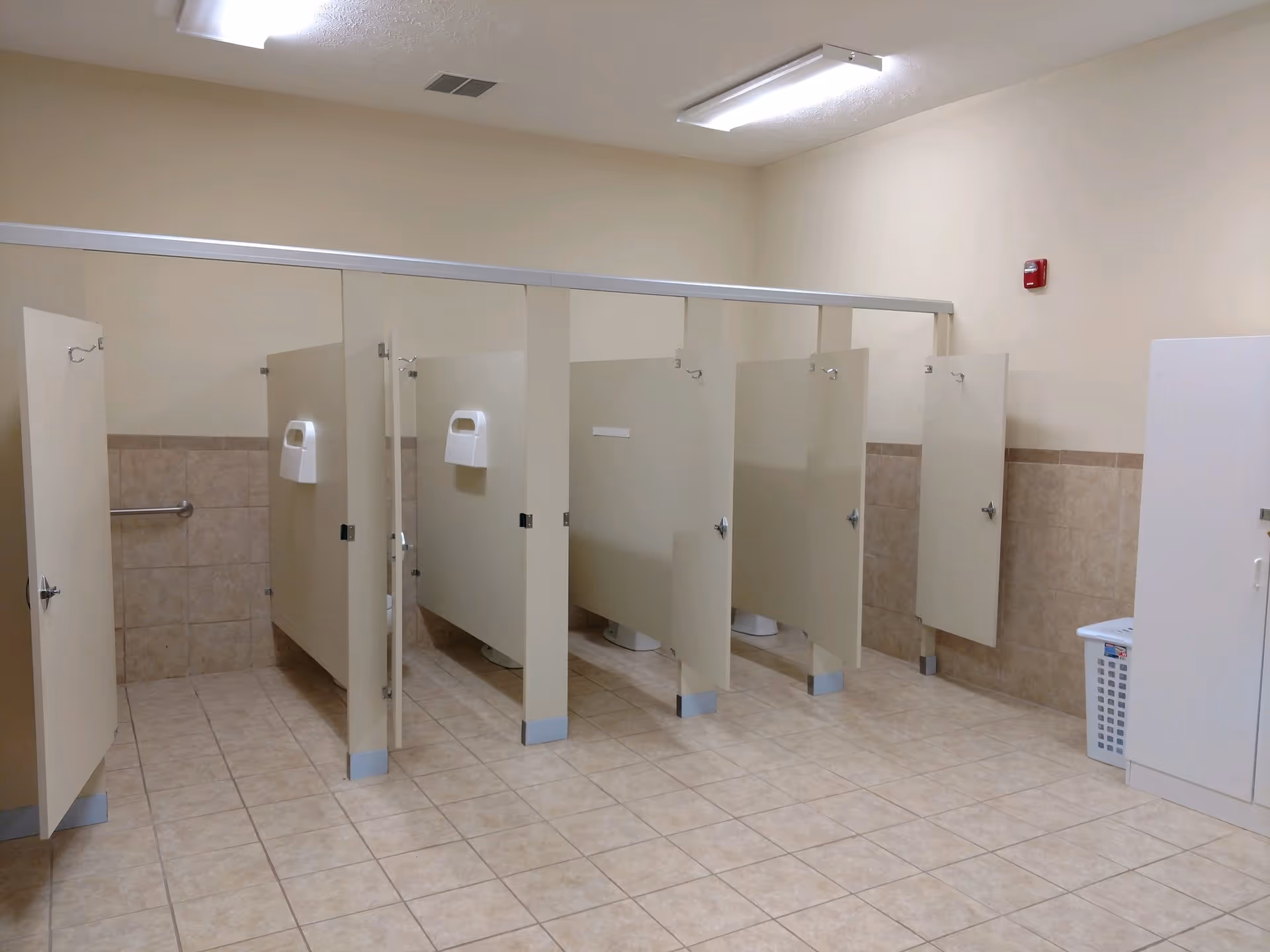 A tiled public restroom with a row of beige toilet stalls and several open stall doors.