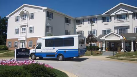 Exterior of Springhouse of Pikesville, a white multi-story senior living building with a blue shuttle.