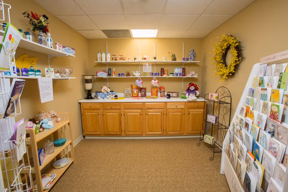Interior gift-shop area with wooden cabinets, wall shelves stocked with snacks and toiletries, and a large display of greeting cards.