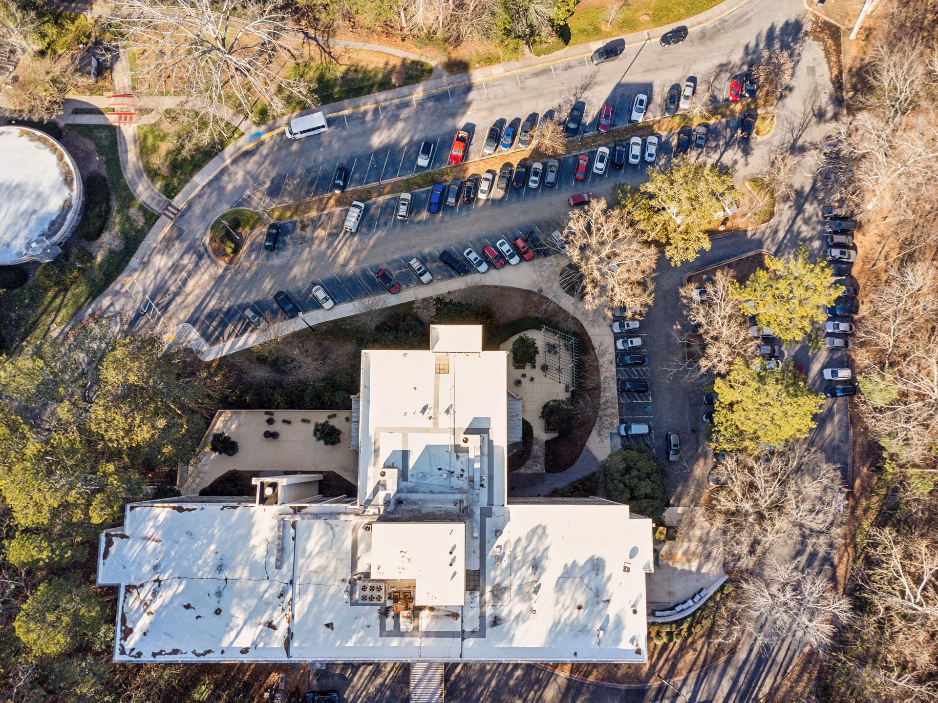 Aerial view of a large white‑roofed nursing and rehab center building with adjacent parking lots, driveways, and surrounding trees.