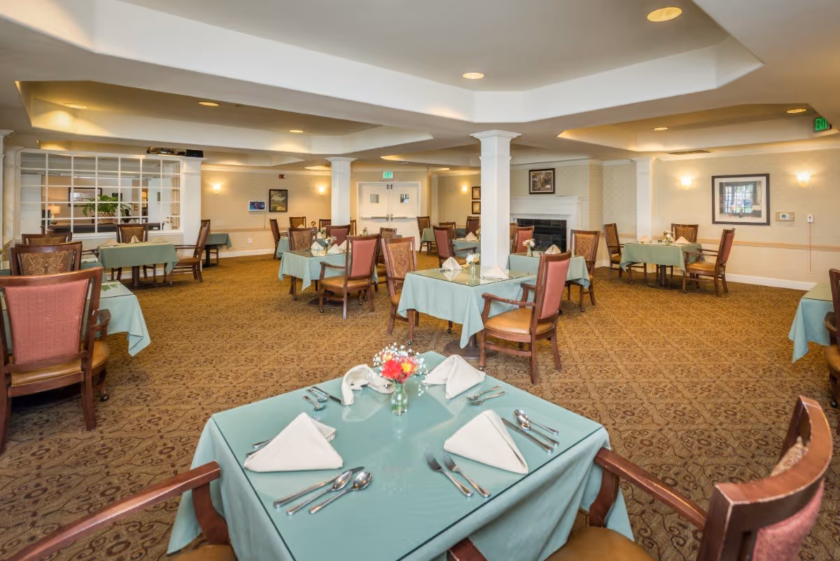 Large dining room with multiple tables set with teal tablecloths, napkins, centerpieces and wooden chairs.
