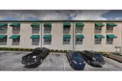 Front facade of a multi-story brick building with green window awnings and cars parked in front.