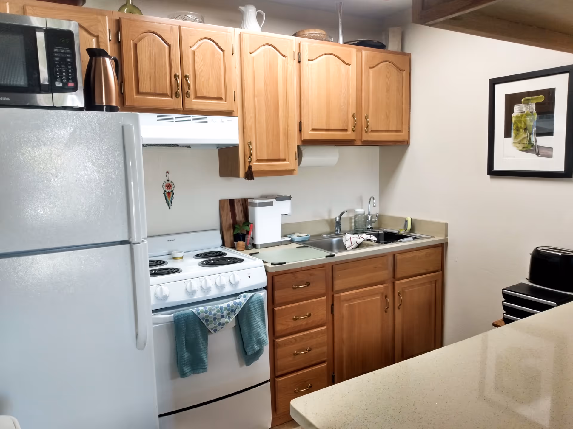 Cozy kitchen with wooden cabinets, a white refrigerator and stove, a sink and countertop, and framed wall art.