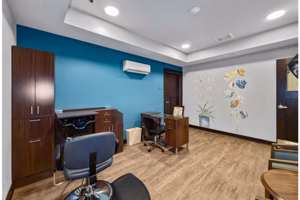 Salon-style interior room with styling chairs, a wash basin, dark cabinetry, a desk, and a decorative hat mural on a blue-accent wall.