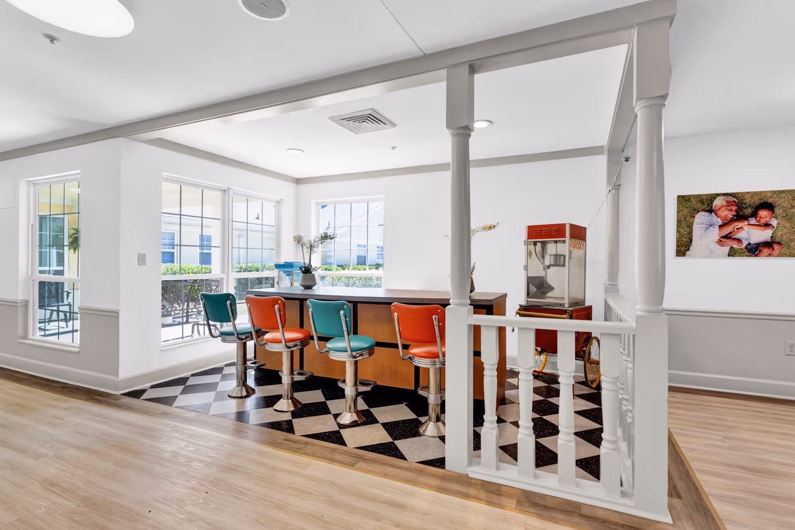 Bright communal area featuring a bar counter with four colorful retro stools beside large windows.