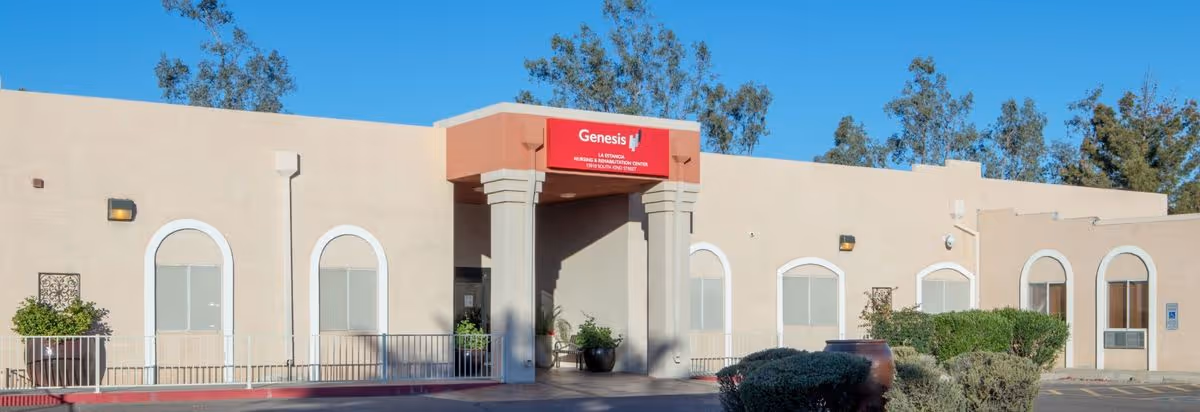 Single-story beige stucco building front with a covered entrance, arched windows, landscaping, and a clear blue sky.