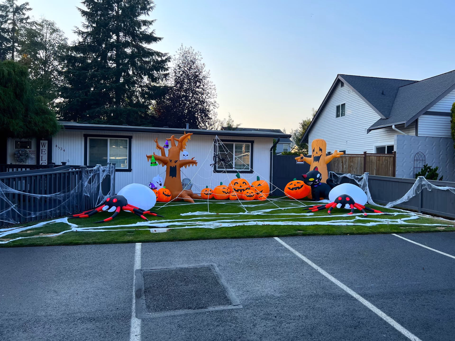 Front yard of a care home decorated for Halloween with inflatable pumpkins, ghosts, spiders and fake cobwebs spread across the lawn and fence in front of the building.