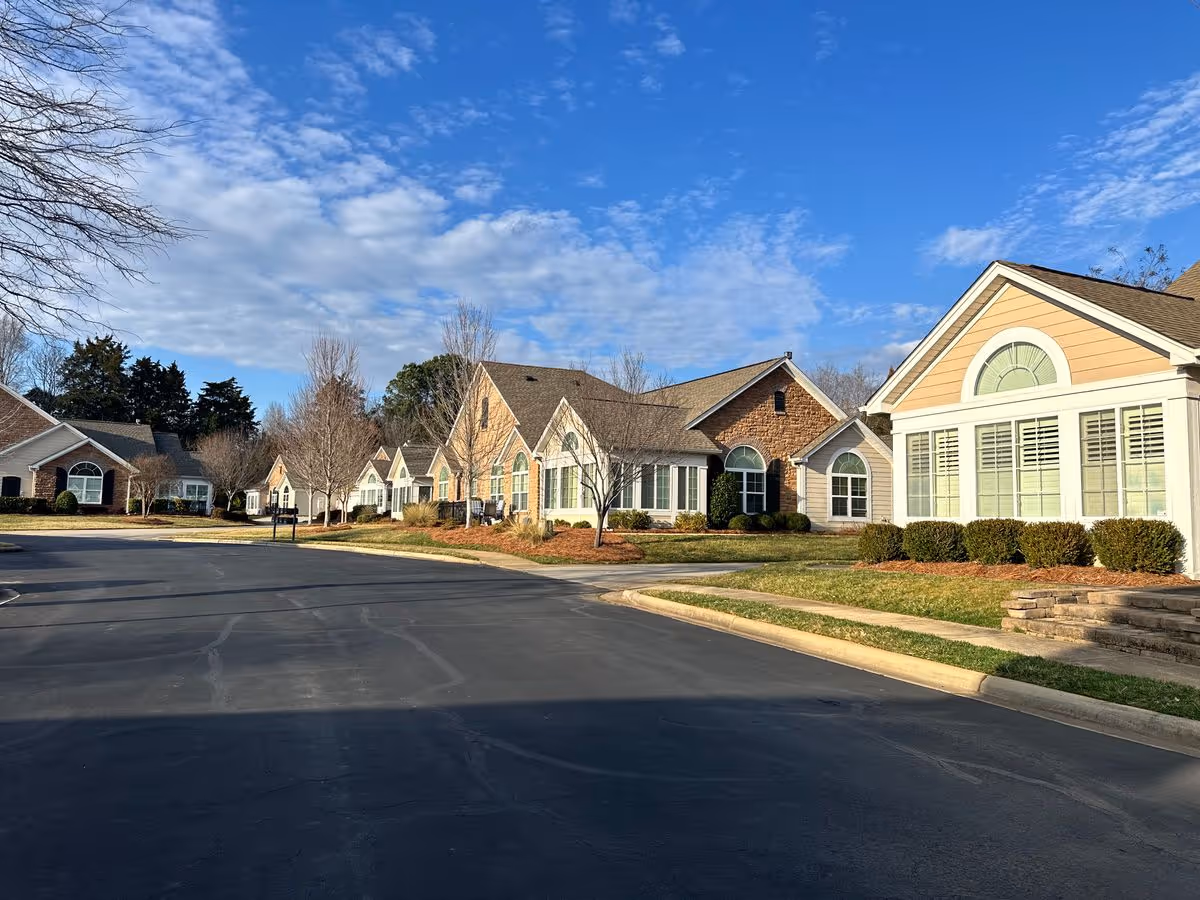 Row of single-story residential buildings with large windows and landscaped lawns under a blue sky.