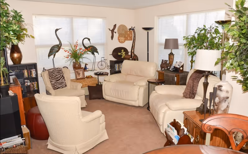 Cozy living room with cream leather sofas and armchairs, decorative plants, wall art, and side tables with lamps.