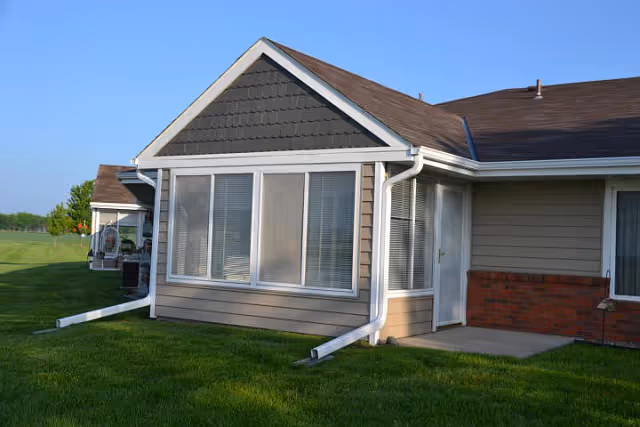 Single-story retirement residence unit exterior featuring large front windows, white gutters, and a well-kept green lawn.