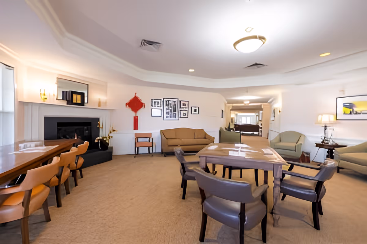 Bright communal dining and lounge room with a central wooden table, surrounding chairs, sofas, and a fireplace.