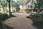 Brick circular courtyard with trees, benches, and a multi-story building in the background.