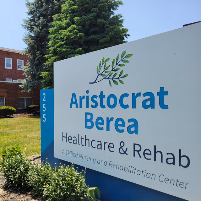 Outdoor sign for Aristocrat Berea Healthcare & Rehab, a skilled nursing and rehabilitation center, with a building and trees in the background.
