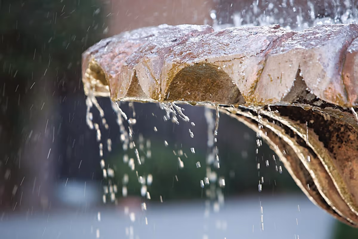 Close-up view of water flowing and dripping from the edge of a stone fountain basin with a blurred background.