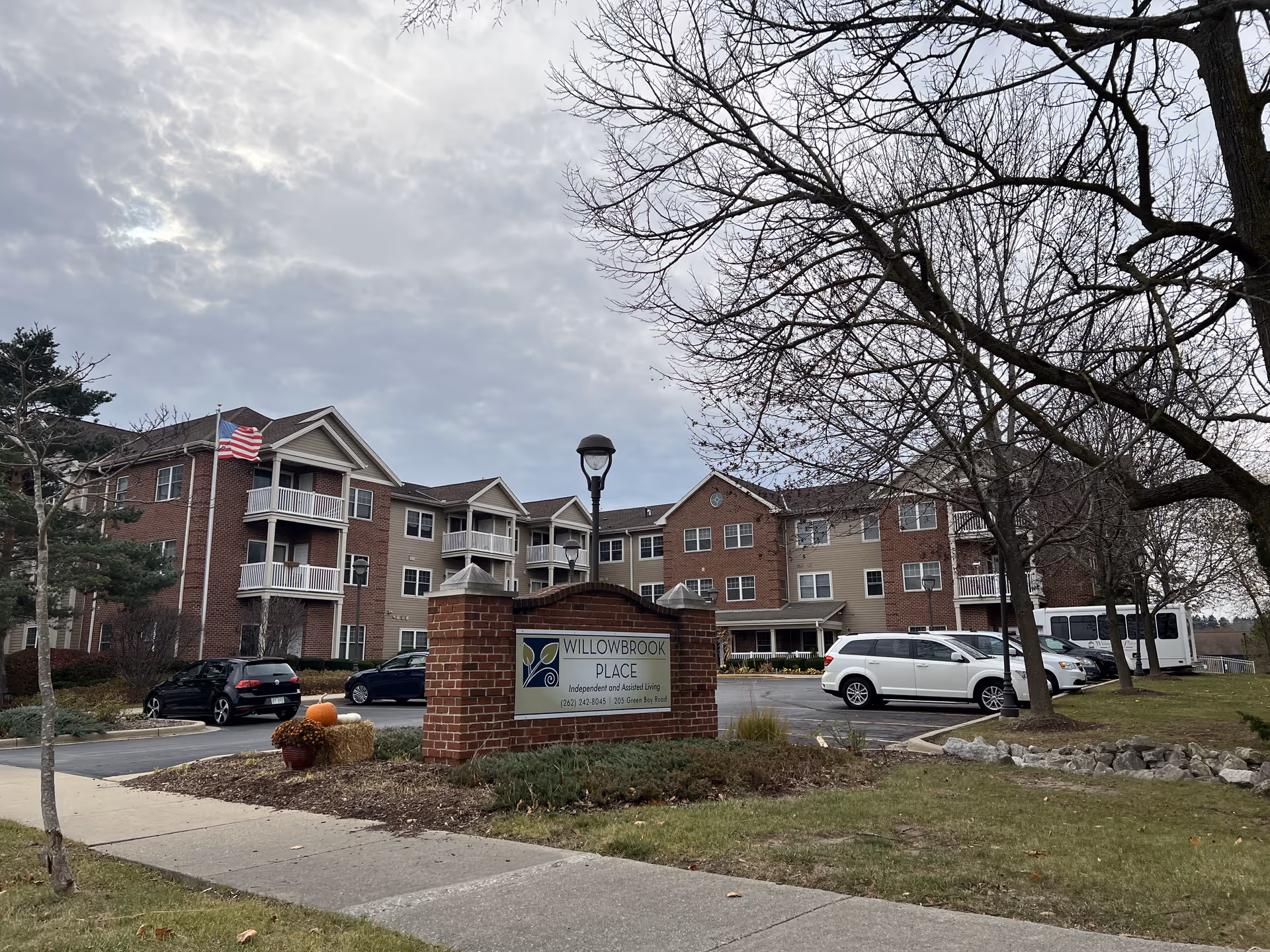 Exterior view of Willowbrook Place senior living facility with parking area and trees.