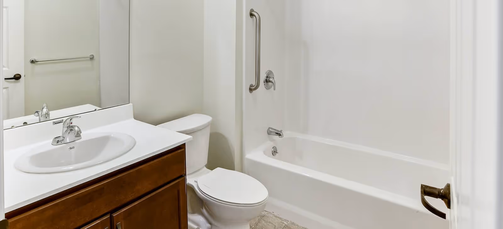 Clean bathroom with a sink vanity, mirror, toilet, and a bathtub with a safety grab bar.