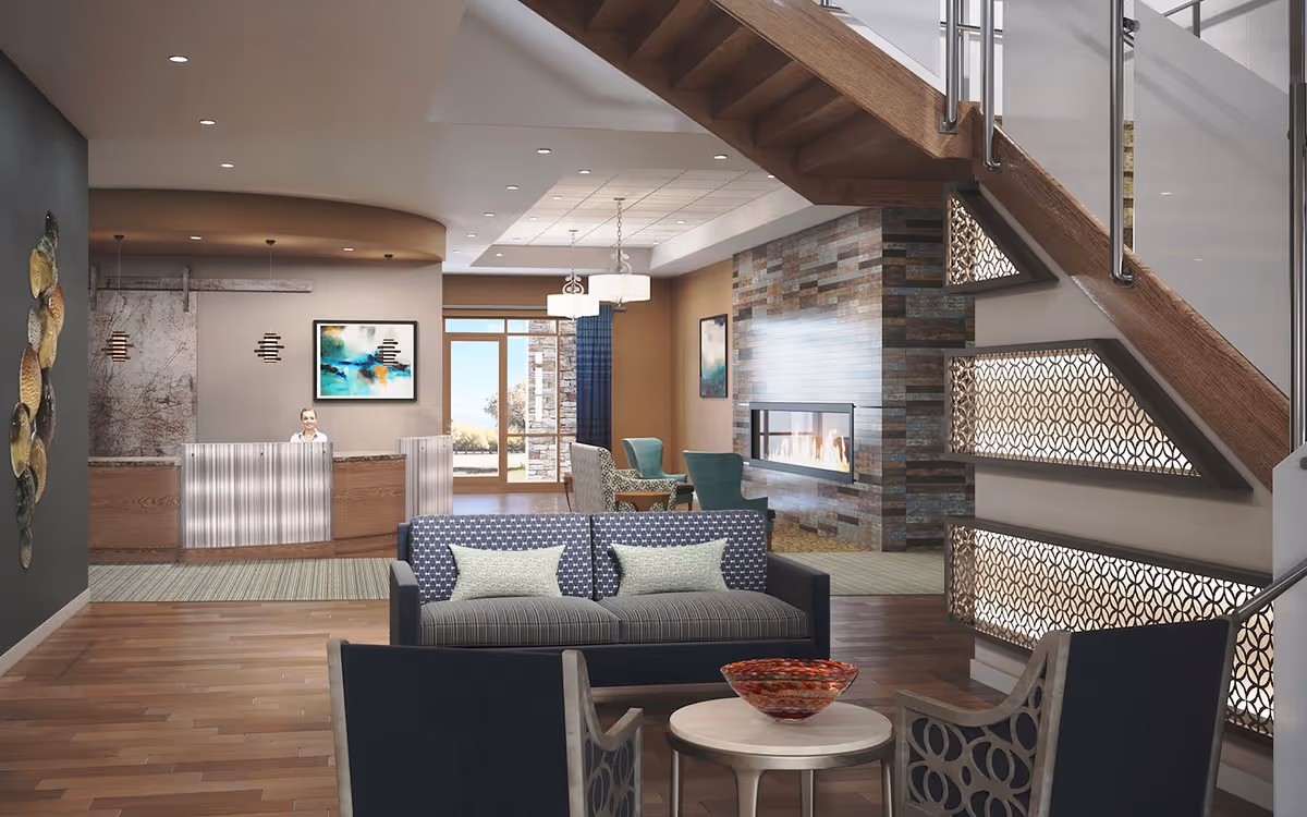 A modern and cozy retirement living lobby with a reception desk on the left, a seating area with a sofa and chairs in the center, a decorative fireplace on the right, and a staircase with illuminated patterned panels underneath. Large windows in the background let in natural light.