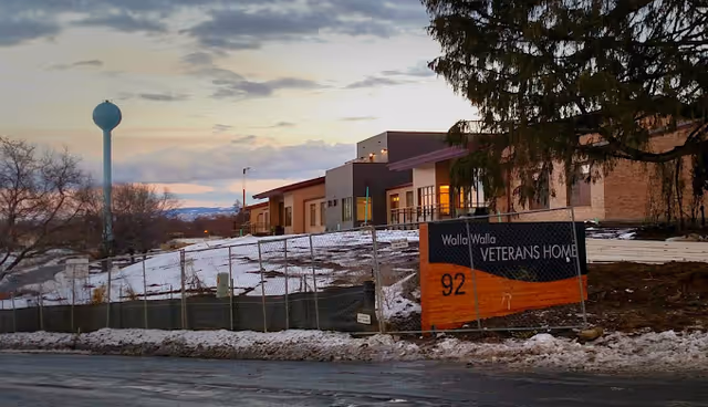 Exterior view of the Walla Walla Veterans Home building and sign with snow-covered ground and a water tower in the background at dusk.