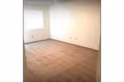 Empty carpeted bedroom with a single window and beige walls.