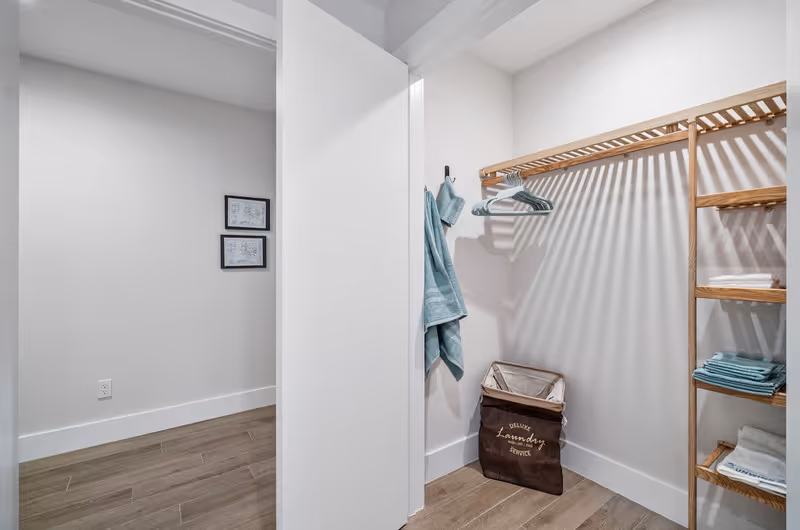 Linen closet with wooden shelves, a hanging rack holding towels and hangers, and a laundry hamper.