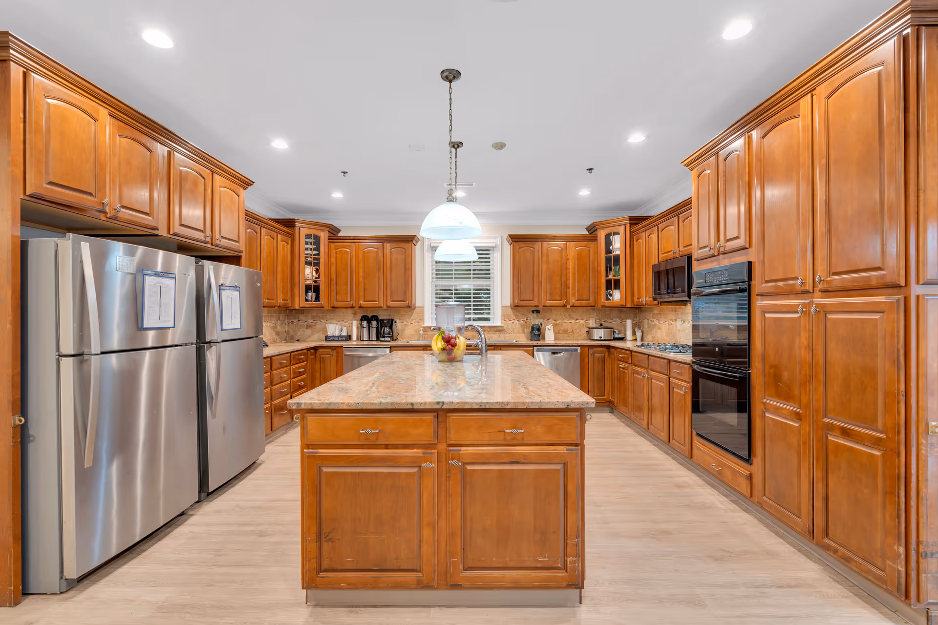 Spacious kitchen with wooden cabinets, a central island, stainless steel refrigerators and pendant lighting.