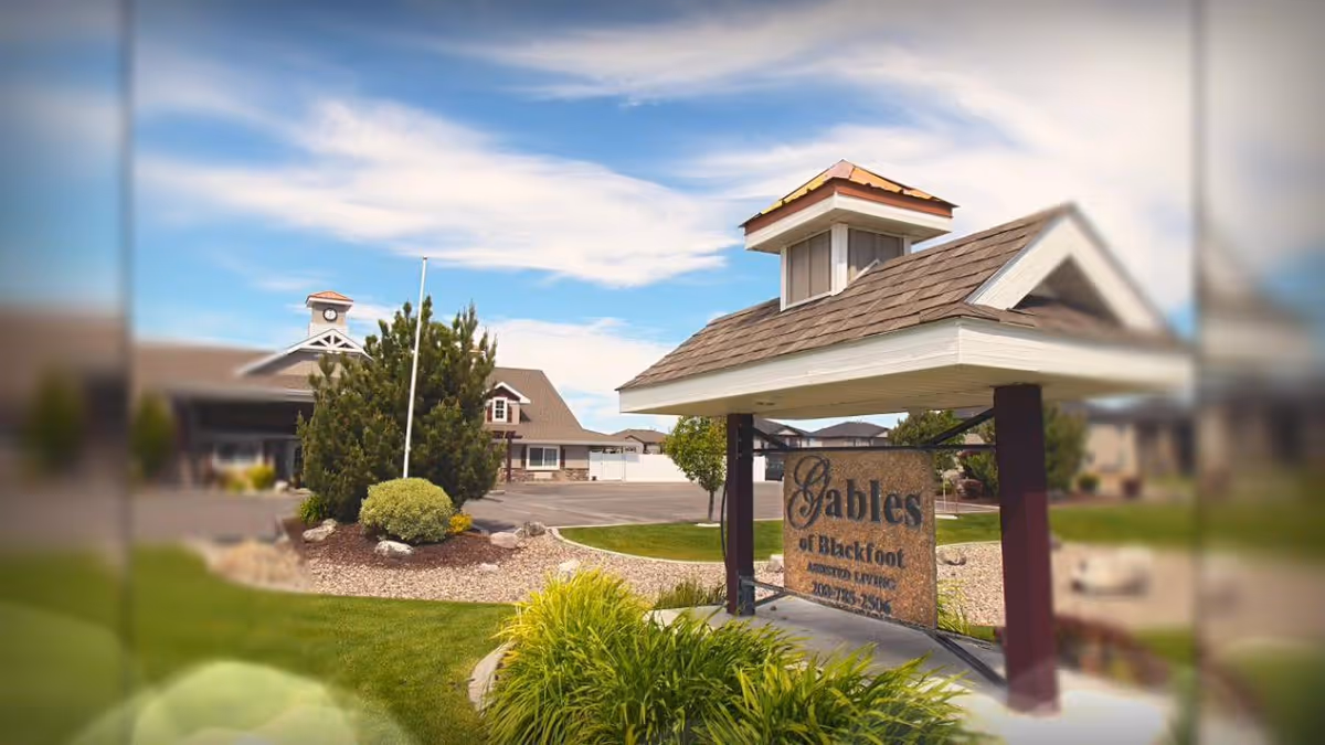 Entrance of a senior living facility with a covered wooden sign reading 'Gables' surrounded by landscaping and the main building in the background.
