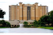A large tan senior living facility with towers beside a pond and fountain.