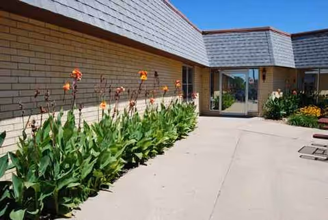 Exterior of a senior living facility with a glass entry door and flowering plants along wall.