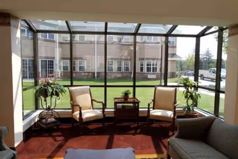 Bright enclosed sunroom with two beige chairs, a small table, and potted plants.