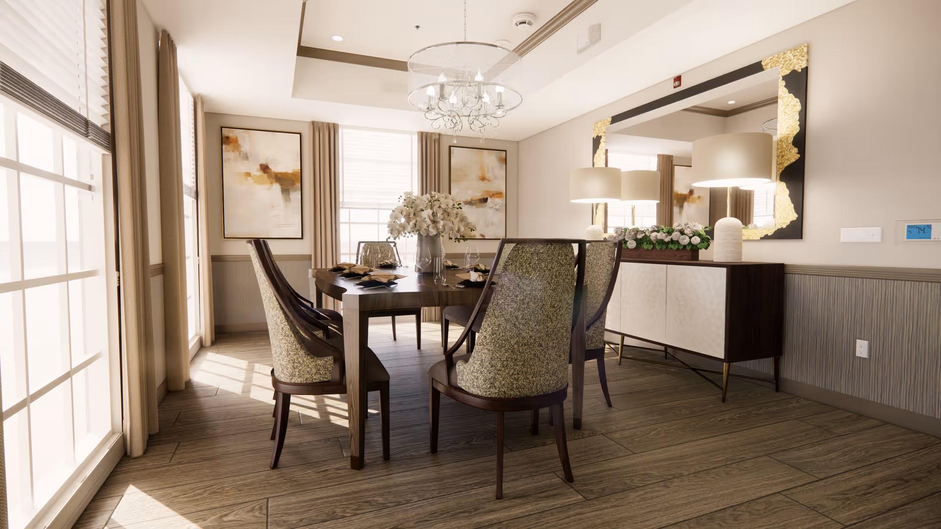 A bright dining room with a wooden dining table surrounded by six upholstered chairs. The table is decorated with a vase of white flowers and place settings. The room features large windows with beige curtains, two abstract paintings on the wall, a chandelier hanging from the ceiling, and a sideboard with a large decorative mirror and two lamps.