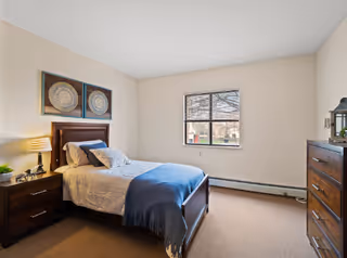 Well-lit bedroom with a single bed, nightstand, dresser, window, and wall art.