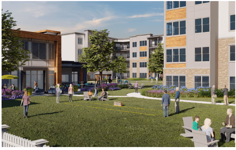 People socialize on a landscaped grassy courtyard with lawn games in front of multi-story senior living buildings.