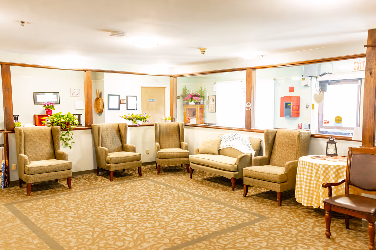 Bright common lounge with several upholstered armchairs, a small sofa, a side table with a checkered cloth, and potted plants.
